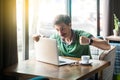 Young angry businessman in green t-shirt sitting with aggressive face and boxing fists and try to punching his laptop Royalty Free Stock Photo