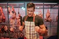 Young angry man stand in front of meet shelf in grocery store. He hold butcher knife in hand and pose. Guy maddly look Royalty Free Stock Photo