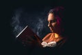 Portrait of young angry woman slapping a dusty book on black background low key