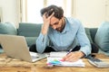 Angry man paying bills as home with laptop and calculator