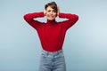 Young annoyed tired lady in red sweater and jeans sadly closing ears with hands over blue background isolated