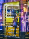 Young anonymous woman taking a Tram in Milan at night. Lombardy, Italy. View through the reflection of the storefront of a bar