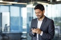 Young arab businessman holding phone, man inside office at workplace typing message and browsing online sites, worker Royalty Free Stock Photo