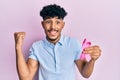 Young arab handsome man holding pink cancer ribbon screaming proud, celebrating victory and success very excited with raised arm Royalty Free Stock Photo