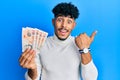 Young arab handsome man holding 10 united kingdom pounds banknotes pointing thumb up to the side smiling happy with open mouth