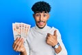 Young arab handsome man holding 10 united kingdom pounds banknotes smiling happy and positive, thumb up doing excellent and