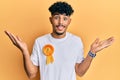 Young arab handsome man wearing fourth place badge celebrating achievement with happy smile and winner expression with raised hand Royalty Free Stock Photo