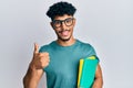 Young arab handsome man wearing glasses and holding books smiling happy and positive, thumb up doing excellent and approval sign Royalty Free Stock Photo