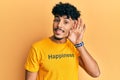 Young arab handsome man wearing tshirt with happiness word message smiling with hand over ear listening and hearing to rumor or