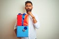 Young arab indian hispanic man holding birthday gifts standing over isolated white background serious face thinking about Royalty Free Stock Photo