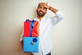 Young arab indian hispanic man holding birthday gifts standing over isolated white background stressed with hand on head, shocked Royalty Free Stock Photo