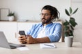 Young Arab Male Entrepreneur Relaxing At Workplace With Smartphone, Browsing Internet