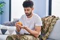 Young arab man army soldier taking pills sitting on sofa at home