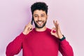 Young arab man with beard having conversation talking on the smartphone doing ok sign with fingers, smiling friendly gesturing Royalty Free Stock Photo