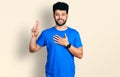 Young arab man with beard wearing casual blue t shirt smiling swearing with hand on chest and fingers up, making a loyalty promise Royalty Free Stock Photo