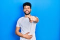 Young arab man with beard wearing casual white t shirt laughing at you, pointing finger to the camera with hand over body, shame Royalty Free Stock Photo