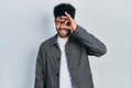 Young arab man with beard wearing glasses doing ok gesture with hand smiling, eye looking through fingers with happy face Royalty Free Stock Photo