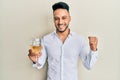 Young arab man drinking a glass of white wine screaming proud, celebrating victory and success very excited with raised arm Royalty Free Stock Photo