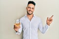 Young arab man drinking a glass of white wine smiling happy pointing with hand and finger to the side Royalty Free Stock Photo