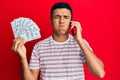 Young arab man having conversation talking on the smartphone holding dollars puffing cheeks with funny face Royalty Free Stock Photo