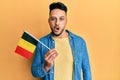 Young arab man holding belgium flag scared and amazed with open mouth for surprise, disbelief face Royalty Free Stock Photo