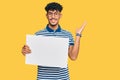 Young arab man holding blank empty banner celebrating victory with happy smile and winner expression with raised hands Royalty Free Stock Photo