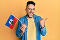 Young arab man holding haiti flag pointing thumb up to the side smiling happy with open mouth