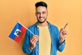 Young arab man holding haiti flag smiling happy pointing with hand and finger to the side