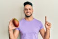 Young arab man holding mango smiling with an idea or question pointing finger with happy face, number one Royalty Free Stock Photo