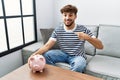 Young arab man holding piggy bank pointing finger to one self smiling happy and proud Royalty Free Stock Photo