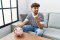 Young arab man holding piggy bank pointing thumb up to the side smiling happy with open mouth Royalty Free Stock Photo
