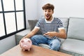 Young arab man holding piggy bank smiling happy pointing with hand and finger Royalty Free Stock Photo