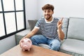 Young arab man holding piggy bank smiling happy pointing with hand and finger to the side Royalty Free Stock Photo