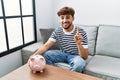Young arab man holding piggy bank surprised with an idea or question pointing finger with happy face, number one Royalty Free Stock Photo