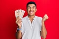 Young arab man holding united kingdom 10 pounds banknotes screaming proud, celebrating victory and success very excited with