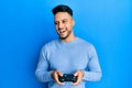 Young arab man playing video game holding controller smiling and laughing hard out loud because funny crazy joke