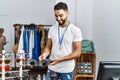 Young arab man shopkeeper paying with credit card and data phone at clothing store