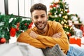 Young arab man smiling happy sitting on the sofa by christmas tree at home Royalty Free Stock Photo