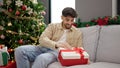 Young arab man unpacking gift with surprised face sitting by christmas tree at home Royalty Free Stock Photo