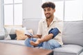 Young arab man using tensiometer sitting on sofa at home