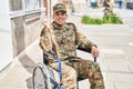 Young arab man wearing camouflage army uniform sitting on wheelchair screaming proud, celebrating victory and success very excited