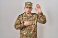 Young arab man wearing camouflage army uniform swearing with hand on chest and open palm, making a loyalty promise oath