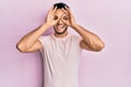 Young arab man wearing casual clothes doing ok gesture like binoculars sticking tongue out, eyes looking through fingers Royalty Free Stock Photo