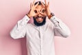 Young arab man wearing casual clothes doing ok gesture like binoculars sticking tongue out, eyes looking through fingers Royalty Free Stock Photo