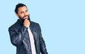 Young arab man wearing casual leather jacket looking confident at the camera smiling with crossed arms and hand raised on chin Royalty Free Stock Photo