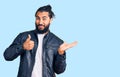 Young arab man wearing casual leather jacket showing palm hand and doing ok gesture with thumbs up, smiling happy and cheerful