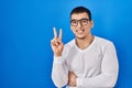 Young arab man wearing casual white shirt and glasses smiling with happy face winking at the camera doing victory sign