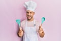 Young arab man wearing professional cook apron and hat holding spoon winking looking at the camera with sexy expression, cheerful Royalty Free Stock Photo