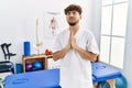 Young arab man working at pain recovery clinic begging and praying with hands together with hope expression on face very emotional Royalty Free Stock Photo