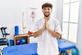Young arab man working at pain recovery clinic praying with hands together asking for forgiveness smiling confident Royalty Free Stock Photo